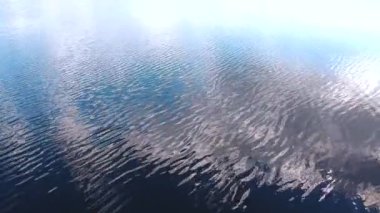 Bulutların yansıdığı bir gölün üzerinde uçuyor. Göldeki sudaki bulutların yansımasının yüksekliğinden bak. Gölde dalgalar, yüksek bir yerden manzara