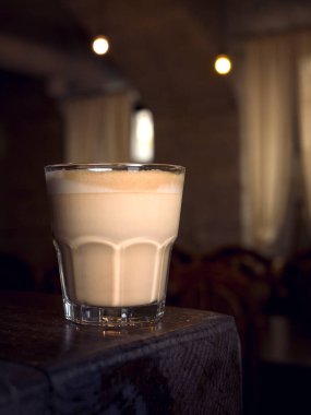 Büyük bardakta kahve. sehpanın üzerinde. Taş duvar. Eski model iç mekan. Kadın elinde kahve tutuyor. Genç kız kahve içiyor. Bardak ahşap masada. retro fotoğraf. 