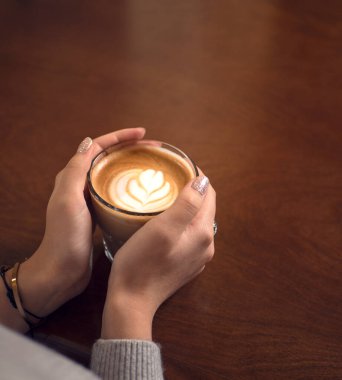 Büyük bardakta kahve. sehpanın üzerinde. Taş duvar. Eski model iç mekan. Kadın elinde kahve tutuyor. Genç kız kahve içiyor. Bardak ahşap masada. retro fotoğraf. 