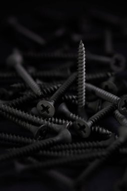 Düz başlı vida yığını ve Phillips sürücüsü, karanlık bir anahtarda.