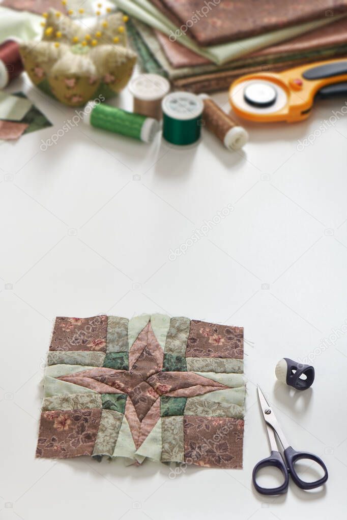 Patchwork block, stack of fabrics, sewing and quilting accessories. Copy space