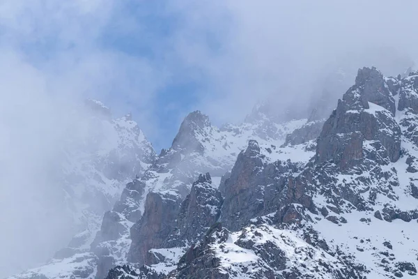 Rocky peaks in snow and fog. Against the background of a blue sky with clouds