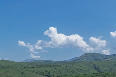 Yeşil dağ tepelerinin tepelerinde beyaz bulutlar. Mavi gökyüzüne karşı