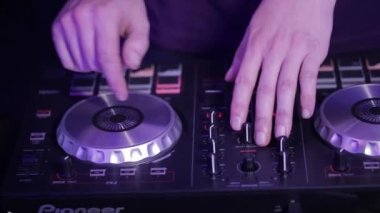 DJ işteymiş. DJ 'in elleri DJ güvertesinde çeşitli parça kontrollerini ayarlar