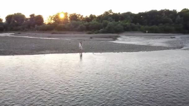 Silhuetas de par encantador perto do rio no pôr do sol — Vídeo de Stock