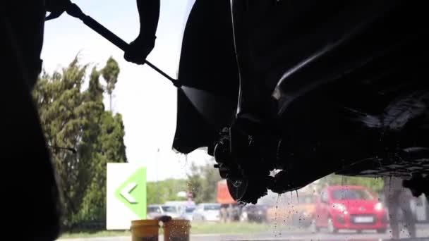 Miespuolinen työntekijä pesee auton. Puhdistus auton avulla korkeapaine vesi. — kuvapankkivideo