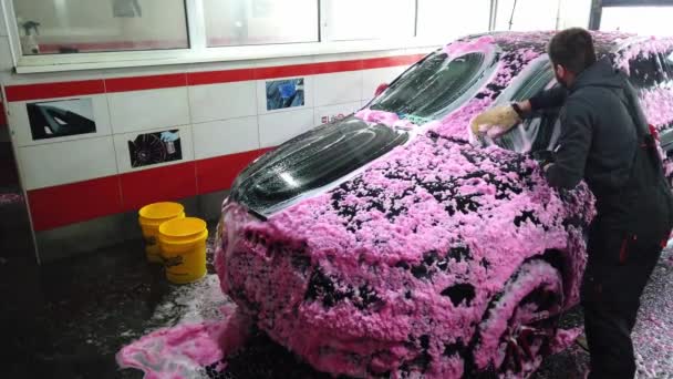 Um homem lava o sedan de uma mangueira especial. Lavagem de carro portátil manual. Cuidados de carro detalhados e gentis Videoclipe