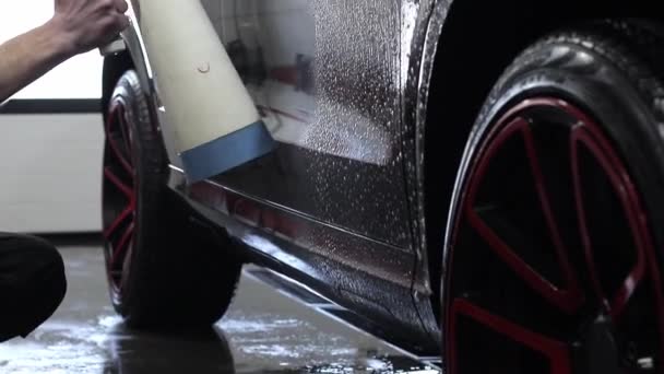 Um homem lava o sedan de uma mangueira especial. Lavagem de carro portátil manual. Cuidados de carro detalhados e gentis — Vídeo de Stock