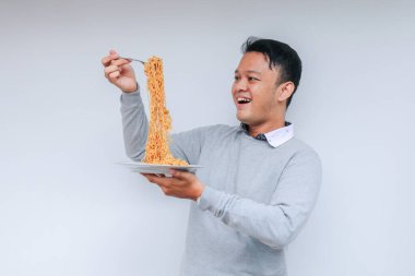 Genç Asyalı mutlu adamın portresi erişteden hoşlanıyor. Öğle yemeği konsepti..