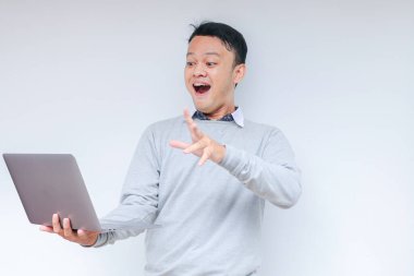 Genç Asyalı adamın yüzü, gri gömlekli, izole edilmiş gri arka planda çalışırken bilgisayarında gördüklerini şok etti..