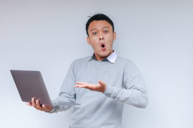 Genç Asyalı adamın yüzü, gri gömlekli, izole edilmiş gri arka planda çalışırken bilgisayarında gördüklerini şok etti..