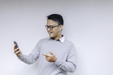 Zeki Asyalı genç adam stüdyo arka planında akıllı telefon kullanırken mutlu ve gülümsüyor.