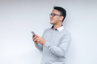 Zeki Asyalı genç adam stüdyo arka planında akıllı telefon kullanırken mutlu ve gülümsüyor.