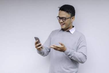 Zeki Asyalı genç adam stüdyo arka planında akıllı telefon kullanırken mutlu ve gülümsüyor.