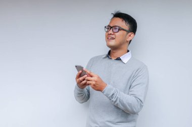 Zeki Asyalı genç adam stüdyo arka planında akıllı telefon kullanırken mutlu ve gülümsüyor.