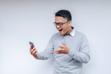 Genç Asyalı adam, gri arka planda gördüğü şey karşısında şok olmuş ve mutlu..