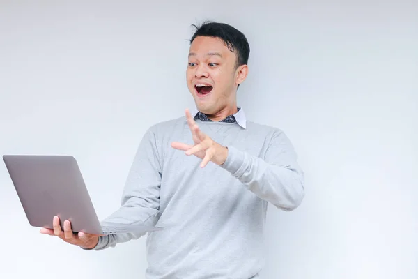 Genç Asyalı adamın yüzü, gri gömlekli, izole edilmiş gri arka planda çalışırken bilgisayarında gördüklerini şok etti..