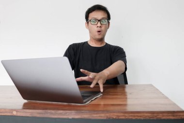 Genç Asyalı adamın yüzü laptopta gördüklerini şok etti. Gri arka planda çalışırken.