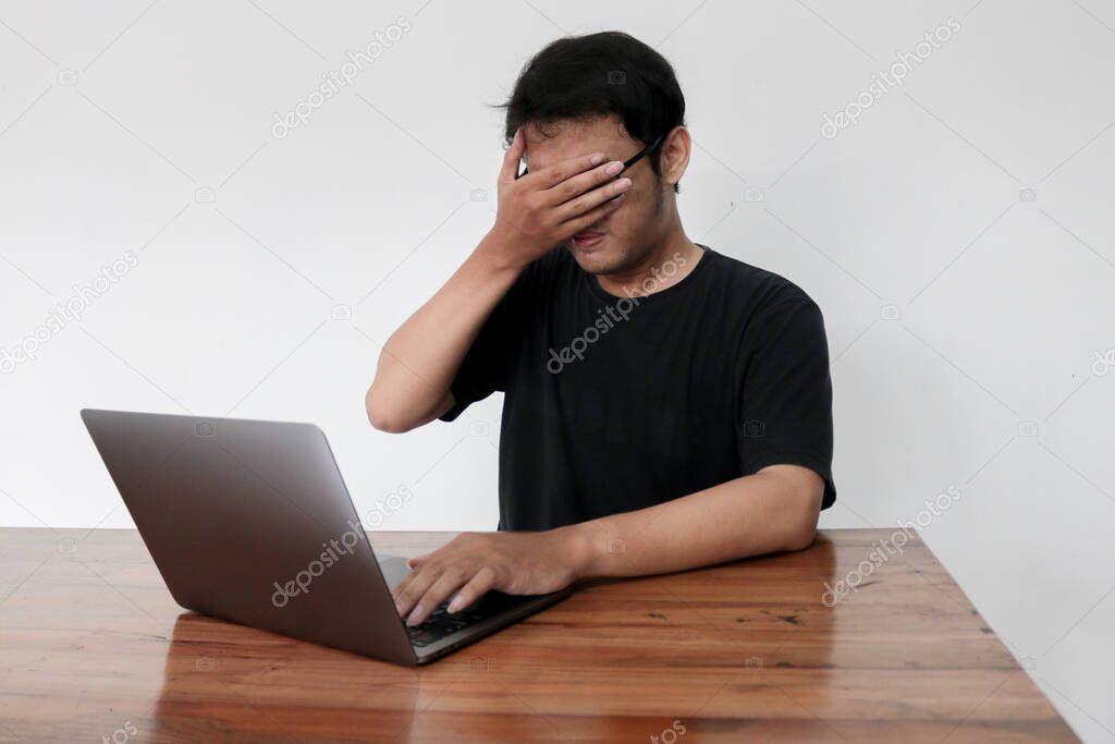 Young asian man hiding his face with hand because shocked and embarrassed by some porn videos or another forbidden thing he saw on the internet using a laptop