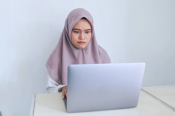 スカーフを被った若いアジア系イスラム教徒の女性は ラップトップを真剣に見ています 灰色の背景のインドネシア人女性 — ストック写真