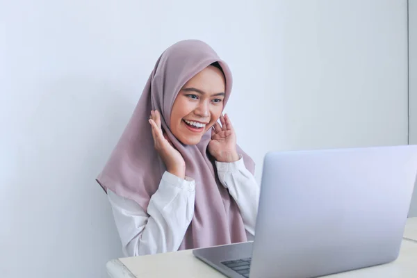 スカーフを被った若いアジア系イスラム教徒の女性は ラップトップでショックと笑顔です 灰色の背景のインドネシア人女性 — ストック写真