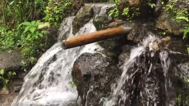 インドネシアのバリ村の農村部の伝統的な素朴な竹や岩から美しい滝のドロップ — ストック動画