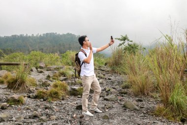 Genç Asyalı sırt çantalı adam dağda seyahat ederken video veya video çekmekten memnun.