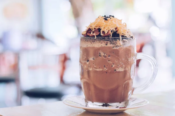 Chocolate Milkshake with chocolate cereals, cheese, and Choco chips in the big clear glass cup. Selective focus close-up on top of it and blurry background.