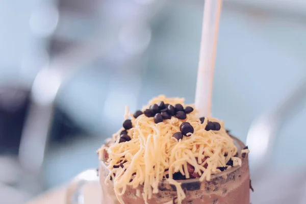 Chocolate Milkshake with chocolate cereals, cheese, and Choco chips in the big clear glass cup. Selective focus close-up on top of it and blurry background.