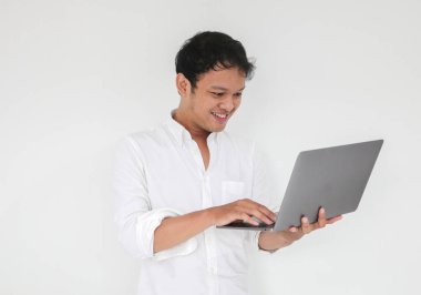 Genç Asyalı adam evde dizüstü bilgisayarla çalışırken gülümsüyor ve eğleniyor. Ev kavramından çalış.