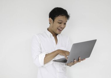 Genç Asyalı adam evde dizüstü bilgisayarla çalışırken gülümsüyor ve eğleniyor. Ev kavramından çalış.