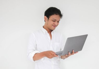 Genç Asyalı adam evde dizüstü bilgisayarla çalışırken gülümsüyor ve eğleniyor. Ev kavramından çalış.