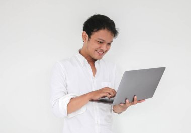 Genç Asyalı adam evde dizüstü bilgisayarla çalışırken gülümsüyor ve eğleniyor. Ev kavramından çalış.