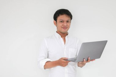 Genç Asyalı adam evde dizüstü bilgisayarla çalışırken gülümsüyor ve eğleniyor. Ev kavramından çalış.