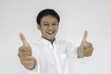 Genç Asyalı adam mutlu gülümseyen yüzü ve baş parmağı olan gri bir gömlek giyer.