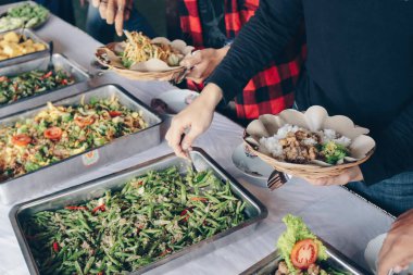 İnsan eli, restoranda öğle yemeği sırasında çelik tavadan ahşap kağıt tabağa beyaz sebzeler koyar.