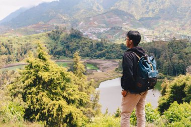 Genç Asyalı sırt çantalı adam mutlu ve dağlarda gezmekten hoşlanıyor..