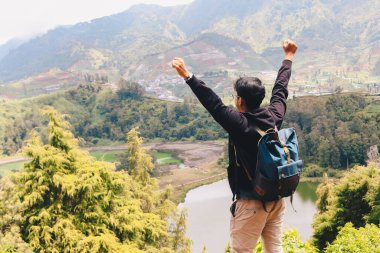 Genç adam bir uçurumun kenarında duruyor ve Dieng Endonezya 'daki dağ ve göl manzarasının tadını çıkarıyor..