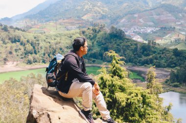 Genç Asyalı sırt çantalı adam mutlu ve dağlarda gezmekten hoşlanıyor..