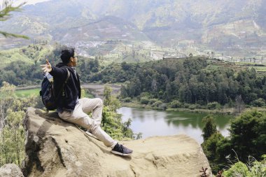 Genç Asyalı sırt çantalı adam mutlu ve dağlarda gezmekten hoşlanıyor..