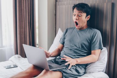 Asyalı adamın rahat yatağında dizüstü bilgisayarıyla çalışmasına şaşırdım ve şok oldum. Başarılı bağımsız yaşam tarzı kavramı.