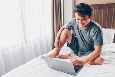 Mutlu Asyalı adam laptopuyla yatağında çalışıyor. Serbest çalışan başarılı yaşam tarzı kavramı.