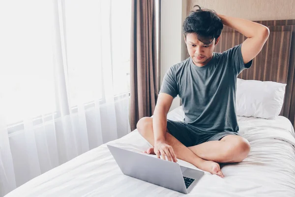 Yatakta dizüstü bilgisayarı olan genç Asyalı adamın kafası karışık ve stresli. Ev kavramından çalış