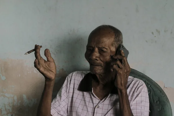 A portrait of Indonesian old grandpa calling in smartphone.