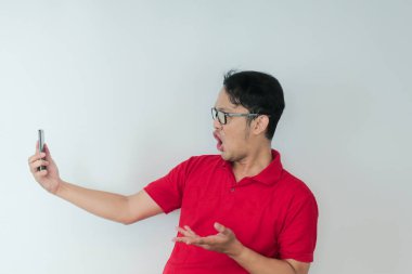 Genç Asyalı adamın yüzü, gri arka planda akıllı telefonda gördüklerini şok etti..