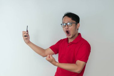 Genç Asyalı adamın yüzü, gri arka planda akıllı telefonda gördüklerini şok etti..