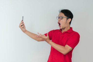 Genç Asyalı adamın yüzü, gri arka planda akıllı telefonda gördüklerini şok etti..