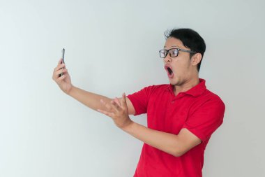 Genç Asyalı adamın yüzü, gri arka planda akıllı telefonda gördüklerini şok etti..