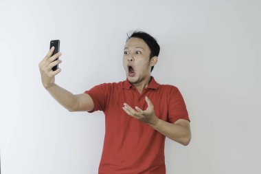 Genç Asyalı adamın yüzü, gri arka planda akıllı telefonda gördüklerini şok etti..