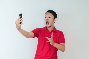 Genç Asyalı adamın yüzü, gri arka planda akıllı telefonda gördüklerini şok etti..